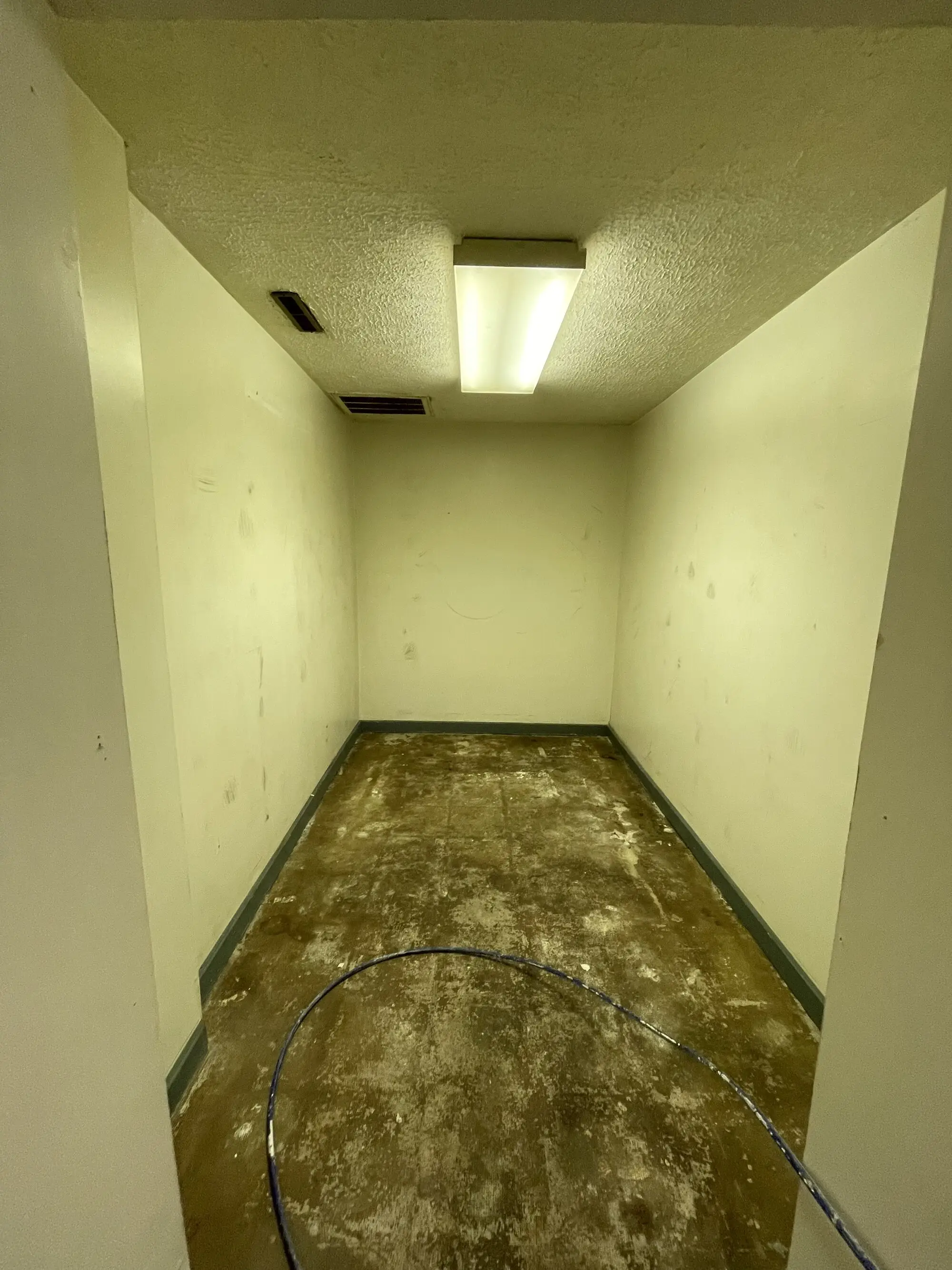 Narrow back room with yellowed walls, a dark green baseboard and a heavily stained concrete floor