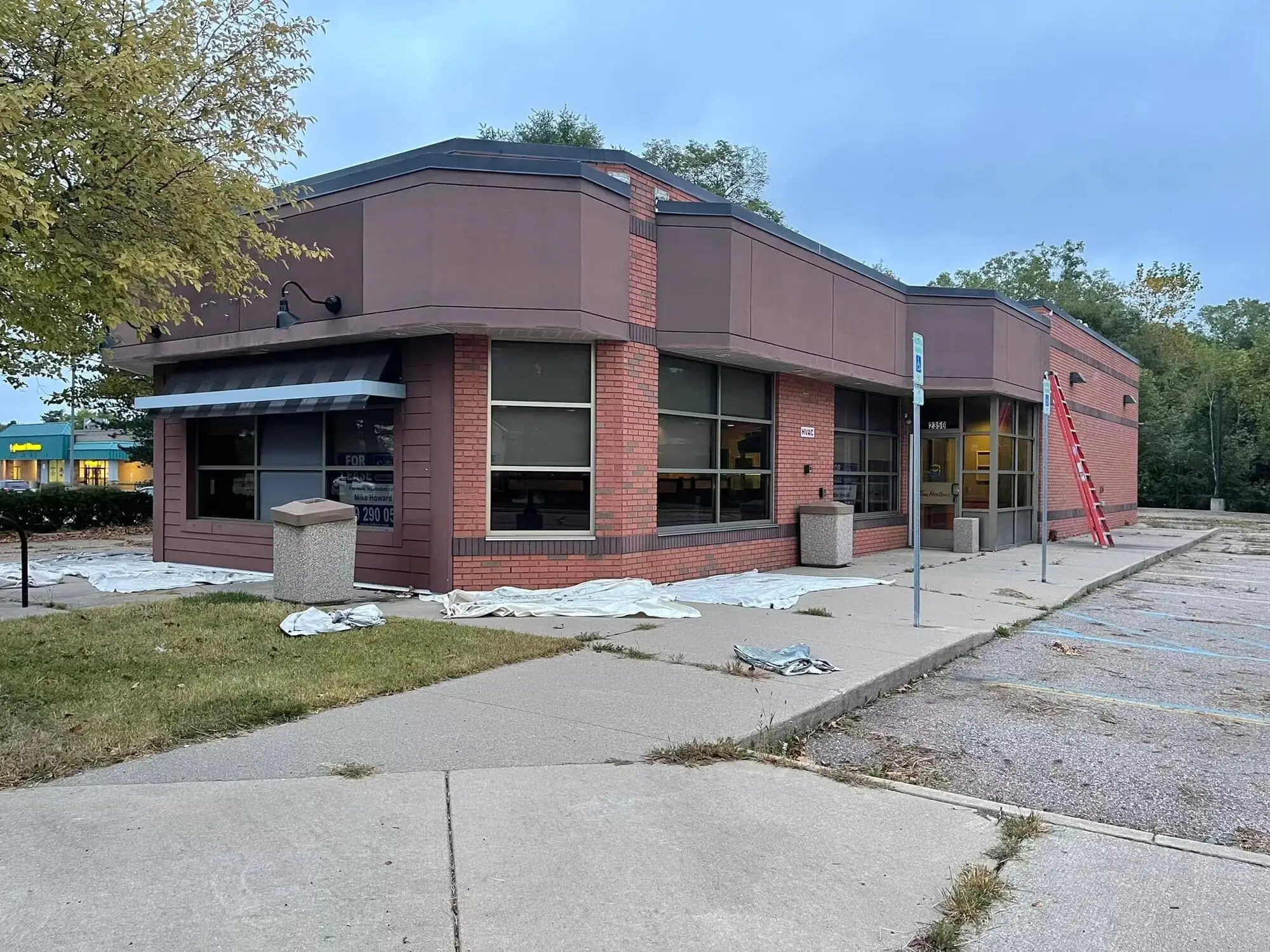 Commercial corner building with a dark maroon upper facade above red brick, drop cloths and a ladder on the walk