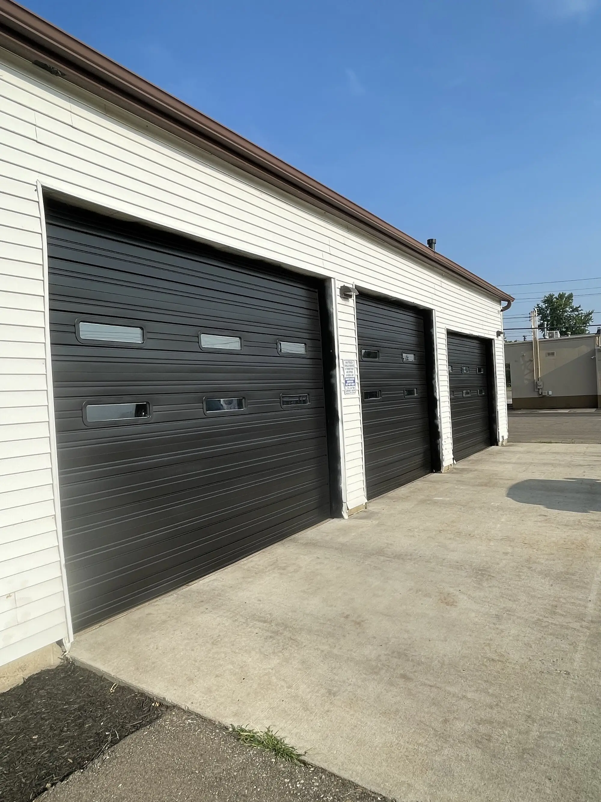 Row of black overhead doors in a white metal commercial building, freshly painted