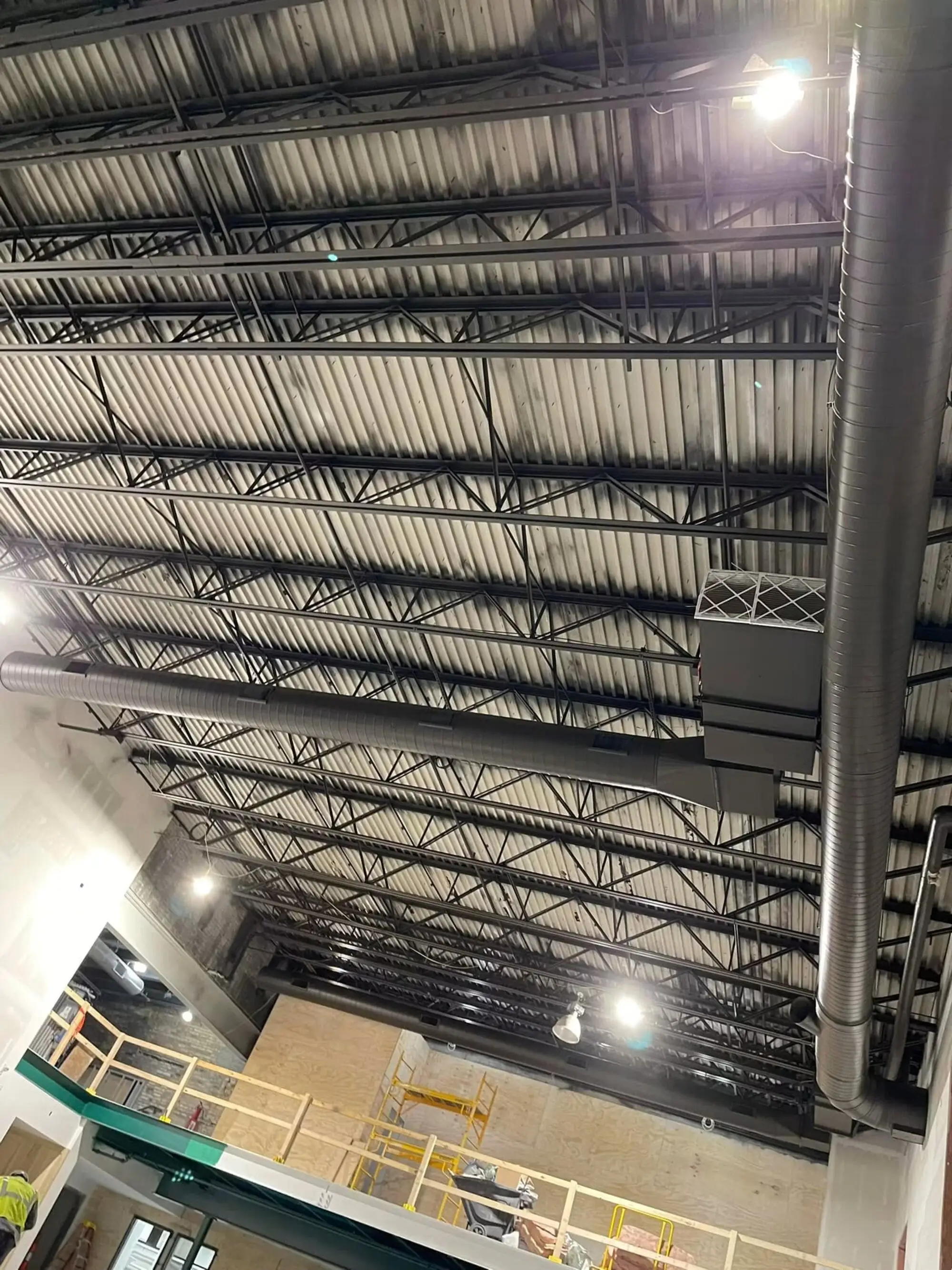 Warehouse ceiling of exposed steel joists, deck and spiral ductwork seen from below