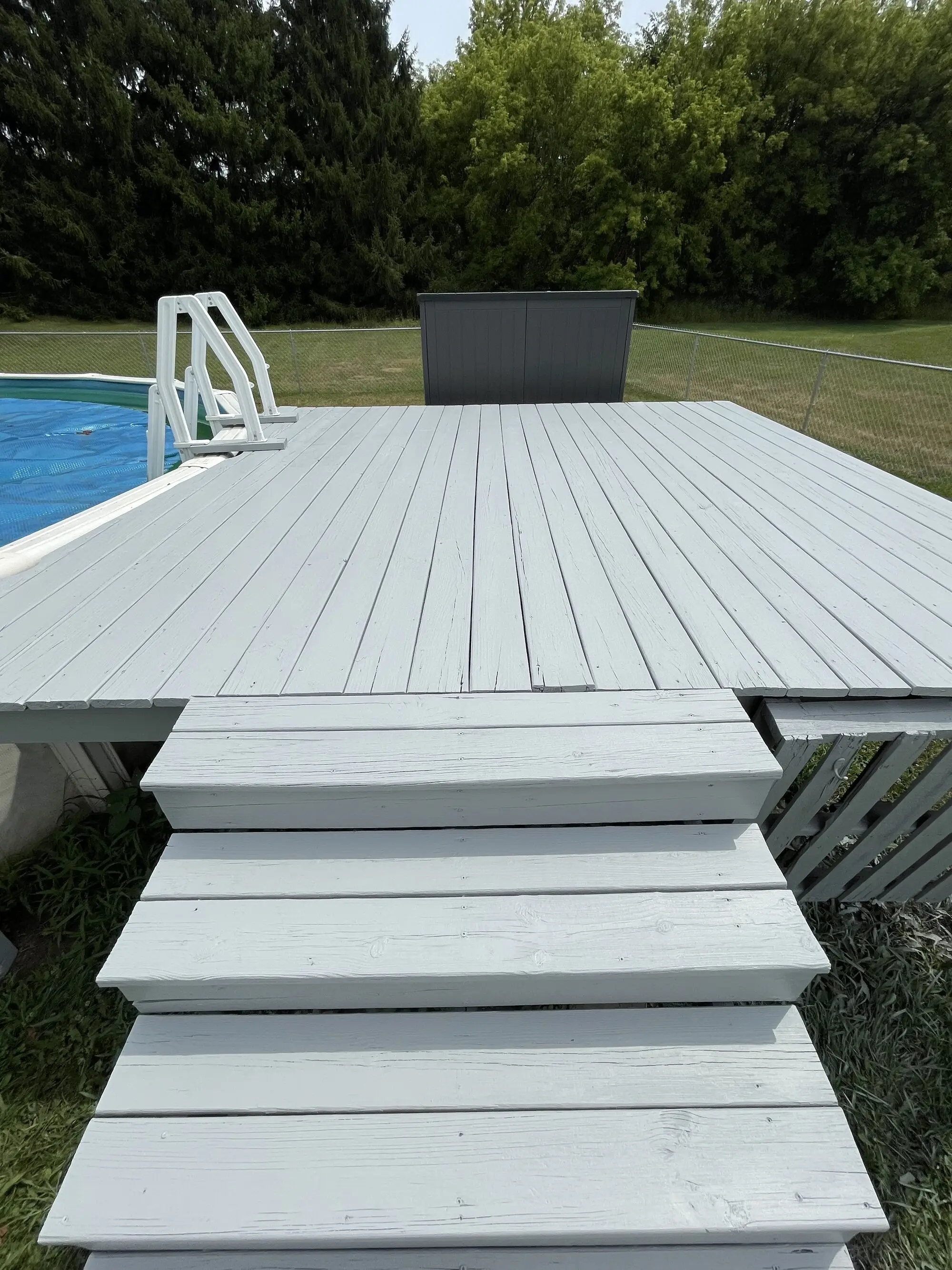 Gray painted pool deck and steps beside an above ground pool