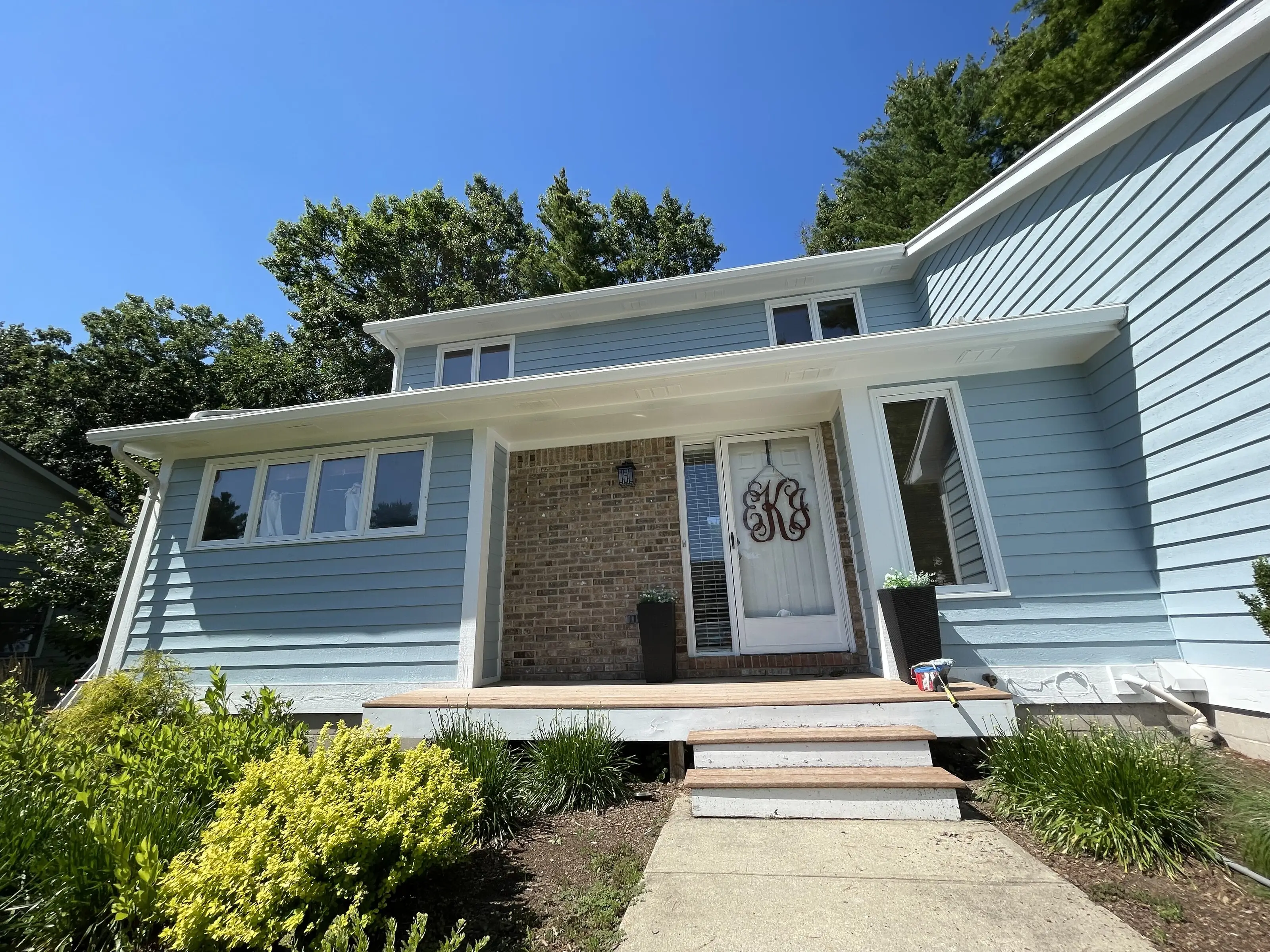 Front entry of a blue sided home with fresh white trim and a monogram on the door