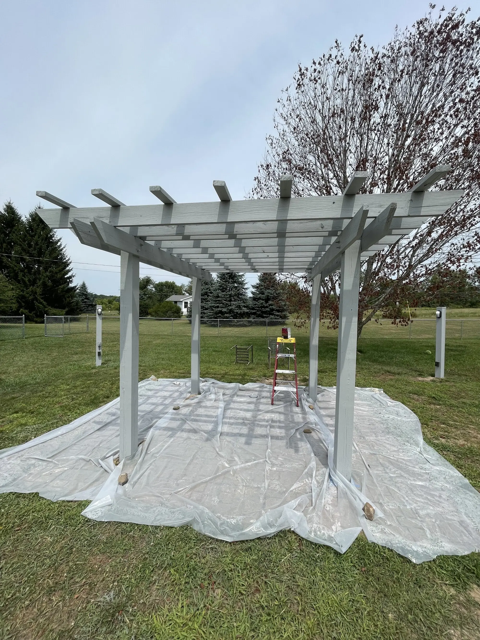 Pergola on a lawn, fully masked out on drop sheets before it is coated