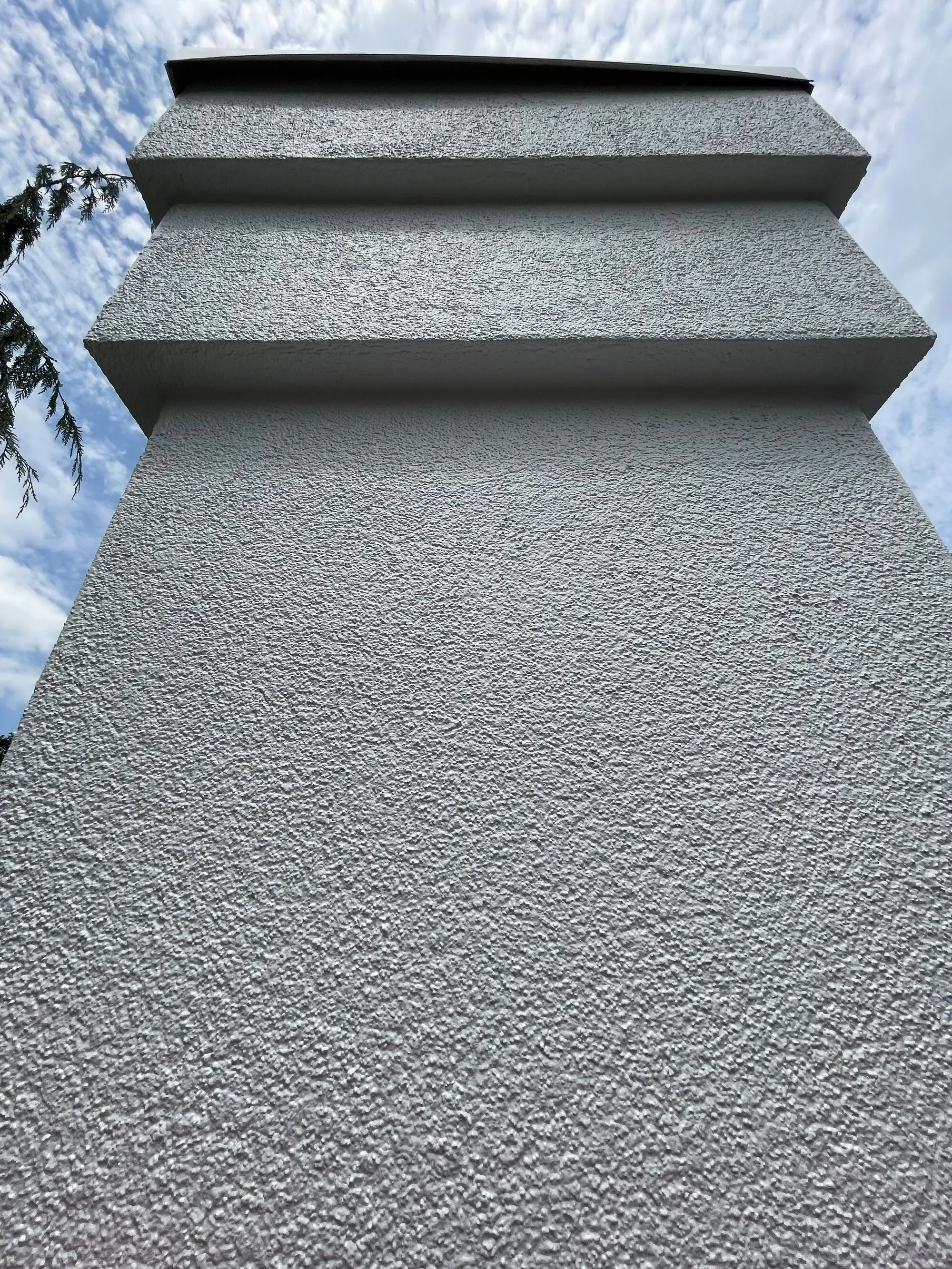 Stucco chimney coated in grey, the banded courses picked out against the sky