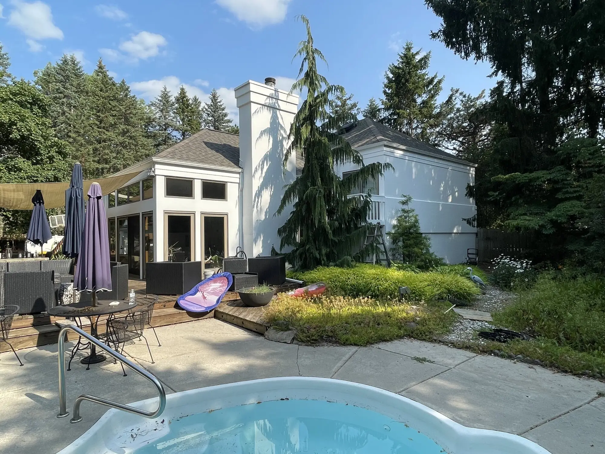 Large white home with a sunroom and chimney seen across the pool deck