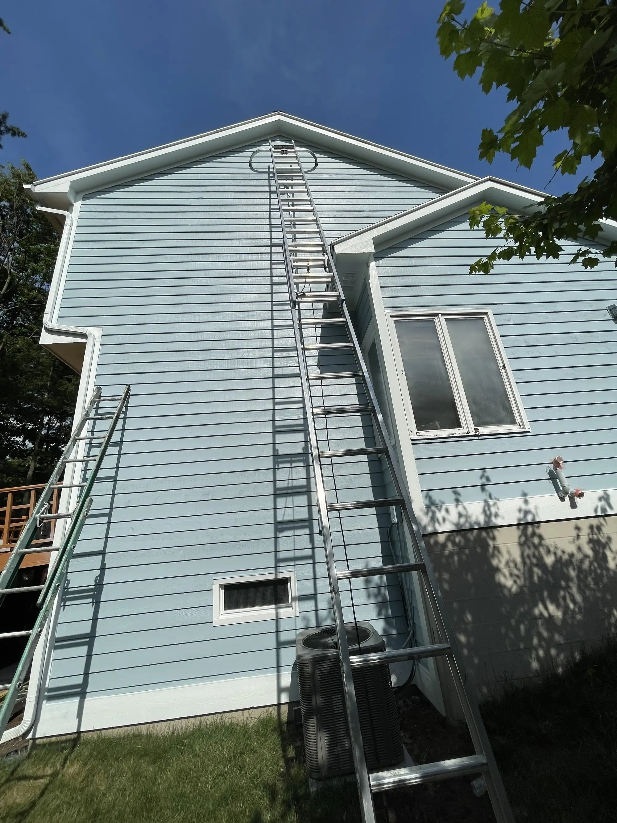 Extension ladders set against the gable end of a pale blue two story home