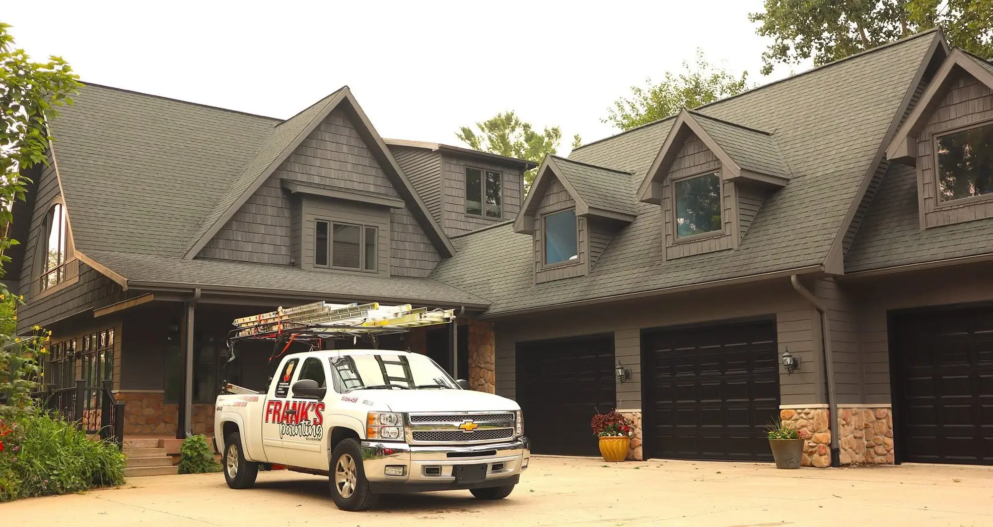 The lettered Frank’s Painting truck with a ladder rack, parked at a large cedar shake home with three garage doors